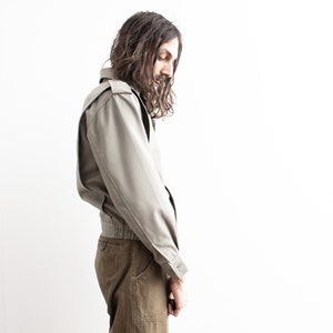 Pu&ograve; includere: Giacca verde oliva chiaro con vestibilit&agrave; bomber. La giacca ha una chiusura con bottoni, spalline e orlo a coste. Il modello indossa pantaloni verde oliva. Lo sfondo &egrave; bianco.