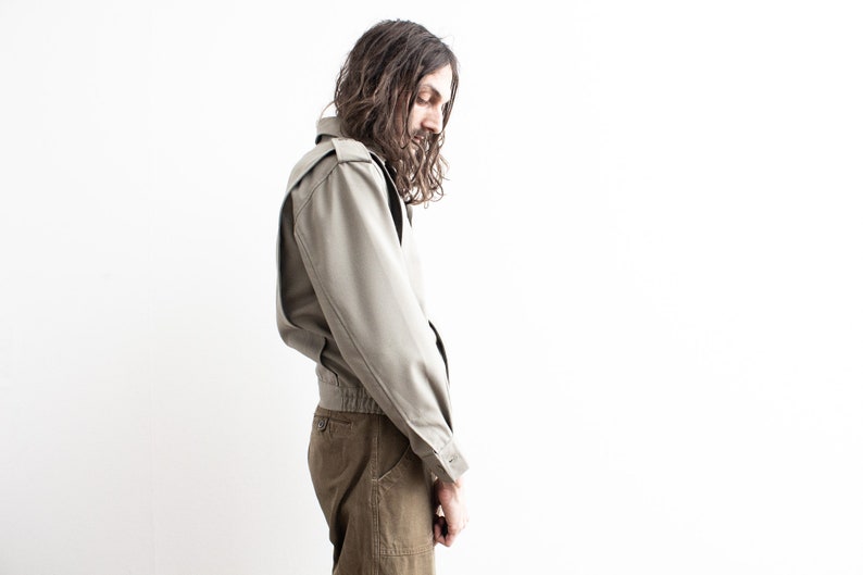 Pu&ograve; includere: Giacca verde oliva chiaro con vestibilit&agrave; bomber. La giacca ha una chiusura con bottoni, spalline e orlo a coste. Il modello indossa pantaloni verde oliva. Lo sfondo &egrave; bianco.