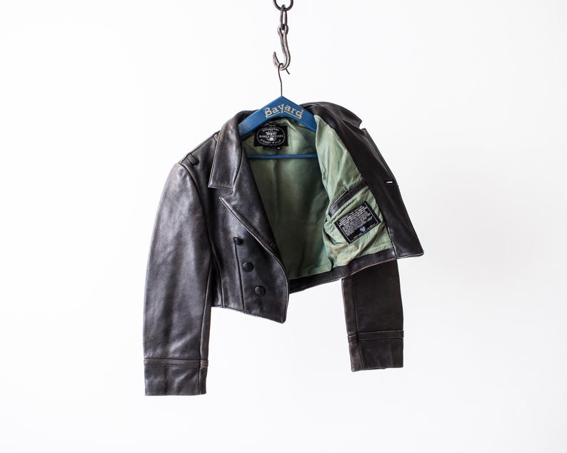 May include: A dark brown leather jacket with a light green interior lining, featuring a notched collar, three black buttons on the front, and a black label inside the lining. The jacket is displayed on a blue hanger labeled Bayard.
