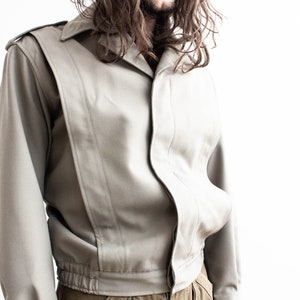 Pu&ograve; includere: Giacca grigio chiaro con colletto e spalline. La giacca presenta un design unico con pannelli verticali e vita elasticizzata. Le maniche sono lunghe e lo stile &egrave; vintage.