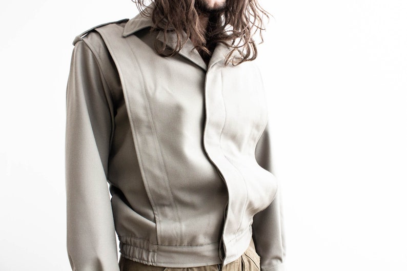 Pu&ograve; includere: Giacca grigio chiaro con colletto e spalline. La giacca presenta un design unico con pannelli verticali e vita elasticizzata. Le maniche sono lunghe e lo stile &egrave; vintage.