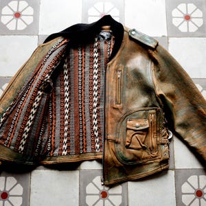 May include: A brown leather jacket with a patterned lining. The jacket has a zip fastening and multiple pockets.