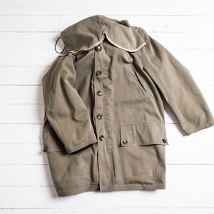 May include: An olive green coat with a large hood and button-up front. The coat has two front pockets and a drawstring around the hood. The coat is made of a durable fabric and appears to be vintage.