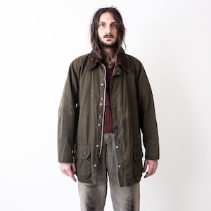 Könnte beinhalten: Olivgrüne gewachste Baumwolljacke mit Cordkragen, Knopfleiste und mehreren Taschen. Die Jacke wird über einem weinroten Pullover und gestreiften Hosen getragen. Ein klassisches Oberbekleidungsstück.