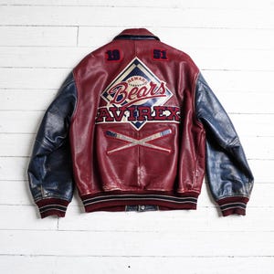 May include: A maroon and blue leather varsity jacket featuring the text Newark Bears and Avirex on the back. The back design includes the numbers 19 and 51, a diamond-shaped logo, and two crossed baseball bats. The jacket has a ribbed collar and cuffs.