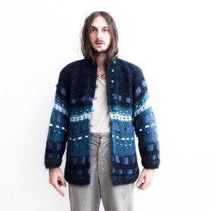 Peut inclure: Un cardigan bleu et noir &agrave; motifs avec un sous-pull blanc et un pantalon gris.