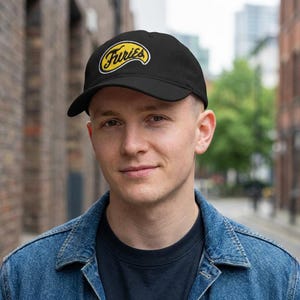 Peut inclure: Une casquette de baseball noire avec un écusson brodé jaune sur le panneau avant. L'écusson a la forme d'une vague stylisée et contient le mot Furies en écriture cursive noire avec une bordure blanche entourant le texte et la forme jaune.