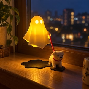 Peut inclure: Une lampe jaune en forme de fantôme avec deux yeux circulaires, reliée par une fine laisse rouge à une petite figurine de chien blanc portant un collier rouge. Le chien se tient sur une base noire en forme de flaque, diffusant une lumière chaude.