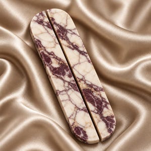 May include: Two elongated, pill-shaped stone pieces featuring a polished surface with a cream-coloured base and deep burgundy veining. The objects are positioned side-by-side, displaying a smooth, rounded edge and a consistent, natural marble pattern.