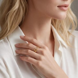 Könnte beinhalten: Ein goldfarbener Metallring mit einem kursiven Schriftzug, der den Namen Emily bildet. Der Ring wird an einem Finger getragen und zeigt die polierte metallische Oberfläche sowie die fließenden, miteinander verbundenen Buchstaben des Namens.