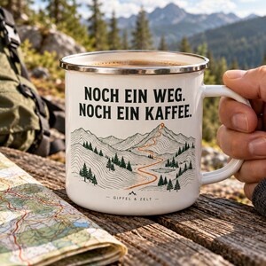 Könnte beinhalten: Ein weißer Emaillebecher mit silbernem Rand, verziert mit einer schwarzen Strichzeichnung einer Berglandschaft und einem geschwungenen orangefarbenen Pfad zum Gipfel. Der Text lautet NOCH EIN WEG. NOCH EIN KAFFEE. sowie GIPFEL & ZELT.