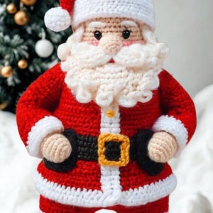 Könnte beinhalten: Eine handgefertigte Häkelpuppe in Form eines Weihnachtsmanns mit rotem Anzug und weißem Besatz, einem schwarzen Gürtel mit gelber Schnalle und einer passenden roten Mütze. Die Figur hat einen dichten weißen Häkelbart, eine runde Nase und schwarze Augen.