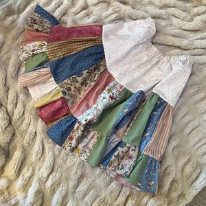 May include: A skirt featuring a patchwork design with various fabric patterns including floral prints, stripes, polka dots, and solid colors in shades of blue, green, pink, brown, and cream. The garment has an elasticized waistband and ruffled tiers.