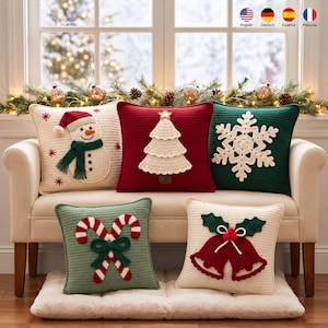 Puede incluir: Cinco cojines cuadrados de ganchillo con diseños navideños: un muñeco de nieve en crema, un árbol de Navidad en rojo, un copo de nieve en verde, dos bastones de caramelo en verde salvia y dos campanas en crema. Cada cojín tiene textura tejida.
