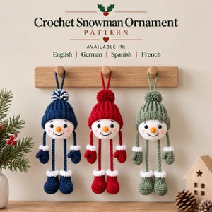 May include: Three crocheted snowman ornaments hanging from a wooden rack. Each snowman features a round white head, orange nose, and a matching hat, mittens, and boots in navy blue, red, or sage green. Text reads: Crochet Snowman Ornament Pattern.