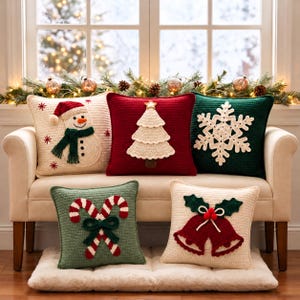 Puede incluir: Cinco cojines cuadrados de ganchillo con motivos navideños: un muñeco de nieve sobre crema, un árbol de Navidad sobre rojo, un copo de nieve sobre verde oscuro, dos bastones de caramelo sobre verde salvia y dos campanas con acebo sobre crema.
