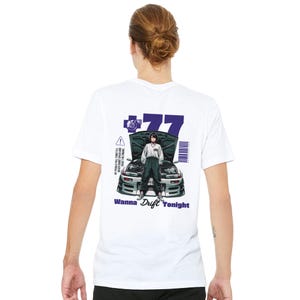 May include: A white t-shirt featuring a graphic on the back of a person standing in front of a car with an open hood. The design includes the number 77, a barcode, and the text "Wanna Drift Tonight" along with "Hit pedals full throttle."