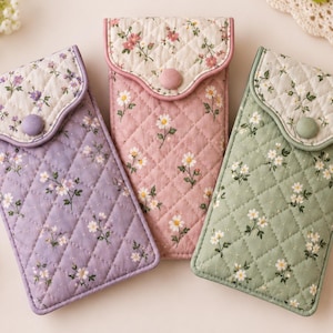 May include: Three rectangular quilted pouches in lavender, dusty pink, and sage green. Each pouch features a cream-colored flap with a floral print, secured by a matching fabric-covered button. The main body of each pouch has a diamond-stitched pattern.