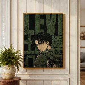Könnte beinhalten: Ein rechteckiger Wandkunstdruck mit einer Anime-Figur mit dunklem Haar und Kapuzenumhang. Der Hintergrund ist dunkel olivgrün mit großem, abgenutztem schwarzem Text, der LEVI und japanische Schriftzeichen zeigt. Goldener Rahmen.