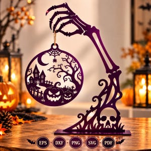 May include: A purple laser-cut display stand featuring a skeletal hand holding a circular ornament. The ornament depicts a haunted house, pumpkins, a spider web, and a crescent moon. The base includes a skull design and text labels EPS, DXF, PNG, SVG, PDF.