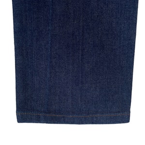 May include: Close-up of the bottom hem of a pair of dark blue denim jeans. The hem is sewn with a straight stitch.