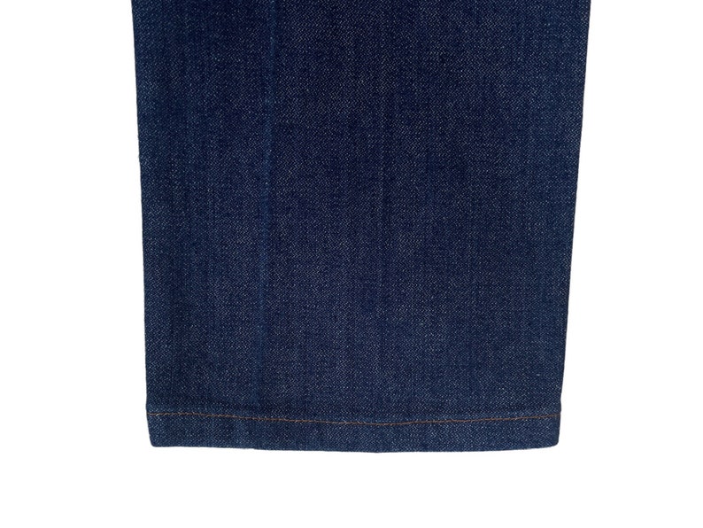 May include: Close-up of the bottom hem of a pair of dark blue denim jeans. The hem is sewn with a straight stitch.