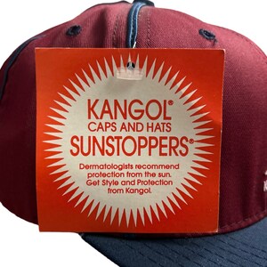 May include: A red and navy blue baseball cap with a white Kangol logo and the text "Caps and Hats Sunstoppers". The tag also includes the text "Dermatologists recommend protection from the sun. Get Style and Protection from Kangol."