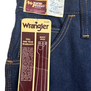 May include: A blue denim Wrangler bootcut jean with a brown label that says "Full One Year Warranty" and "Boot Jean". The label also includes the Wrangler logo and the text "W-439".