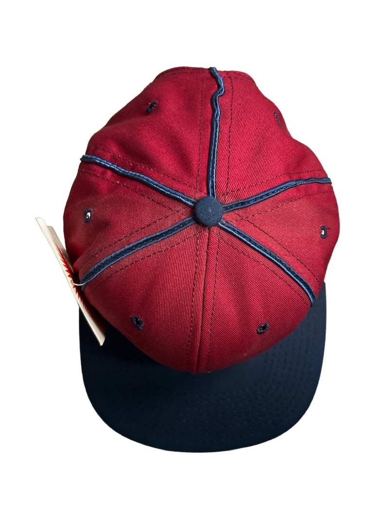May include: A red baseball cap with a navy blue brim and a navy blue stitching detail. The cap has a button on top.