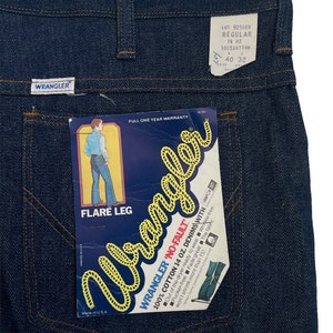 以下が含まれることがあります： フレア レッグの青いデニムのラングラー ジーンズ。ジーンズには、「Wrangler 'No-Fault' 100% コットン 14 オンス デニム with サンフォライズド」と「フレア レッグ」と書かれたラベルが付いています。ラベルには、「ロット 925DEN レギュラー 14 オンス 100% コットン 40 32」とも書かれています。