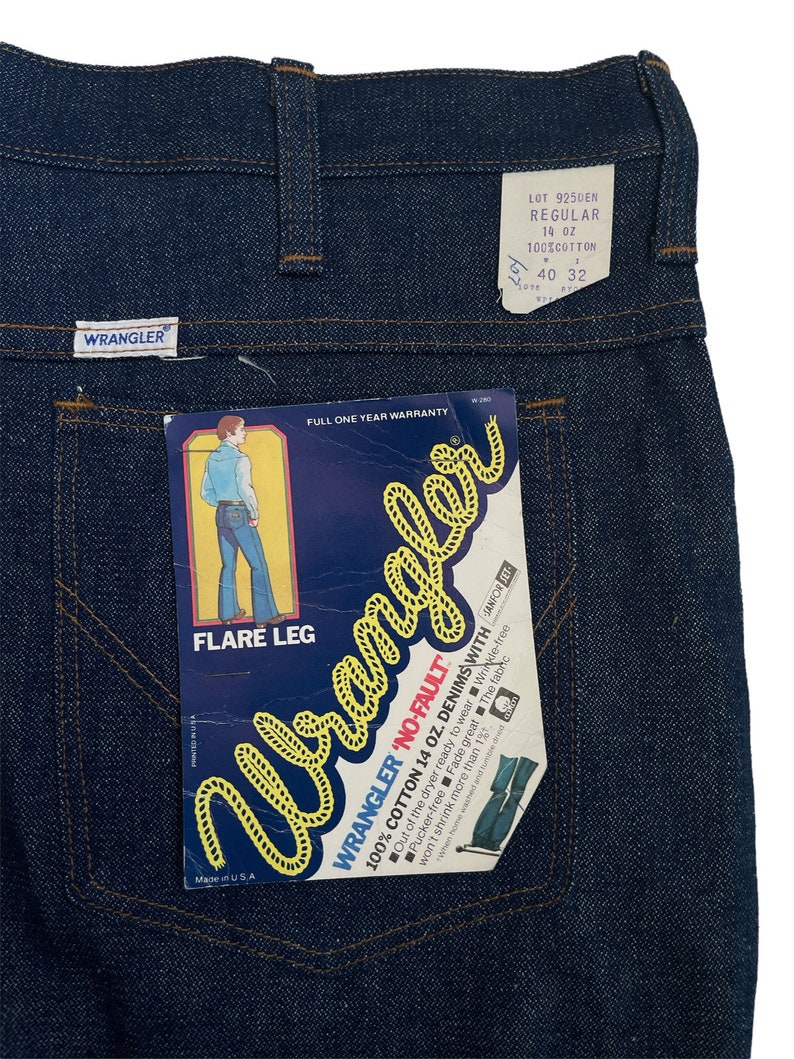 以下が含まれることがあります： フレア レッグの青いデニムのラングラー ジーンズ。ジーンズには、「Wrangler 'No-Fault' 100% コットン 14 オンス デニム with サンフォライズド」と「フレア レッグ」と書かれたラベルが付いています。ラベルには、「ロット 925DEN レギュラー 14 オンス 100% コットン 40 32」とも書かれています。