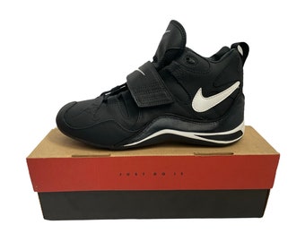 May include: Black and white Nike high-top athletic shoes with a velcro strap. The shoes are on a box with the words "Just Do It" printed on the side.