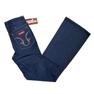 May include: A pair of dark blue denim jeans with a wide leg. The jeans have a high waist and a Wrangler label on the back pocket. The jeans have a yellow stitching detail on the back pockets.