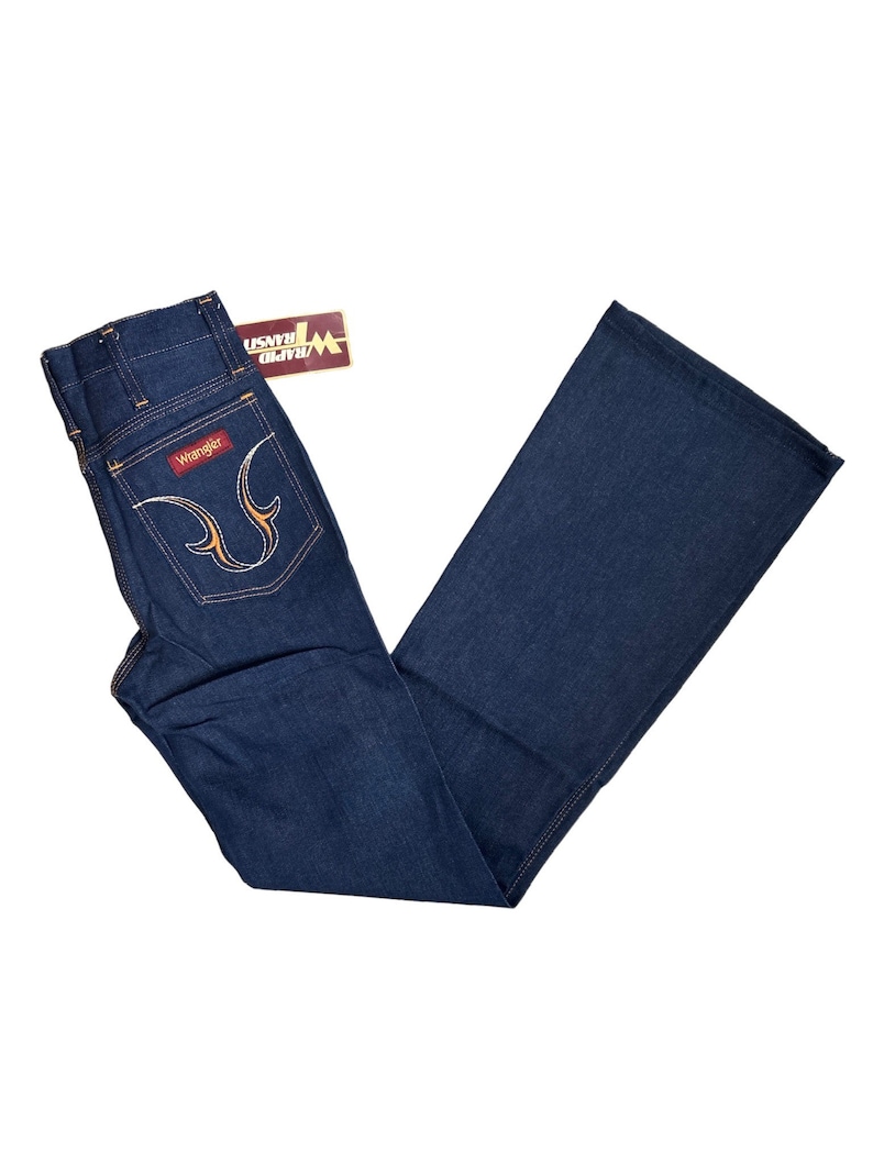 May include: A pair of dark blue denim jeans with a wide leg. The jeans have a high waist and a Wrangler label on the back pocket. The jeans have a yellow stitching detail on the back pockets.