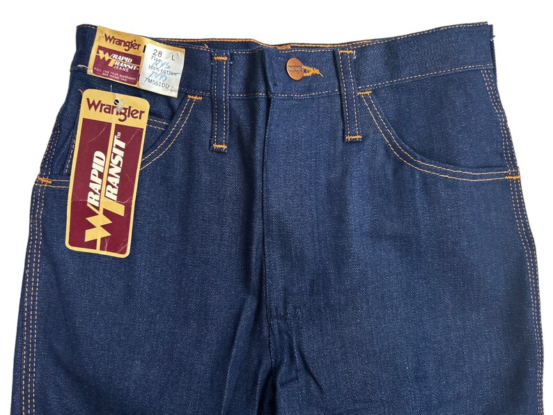 May include: A pair of blue denim jeans with orange stitching. The jeans have a label that says "Wrangler Rapid Transit" and a size tag that says "28" and "L".