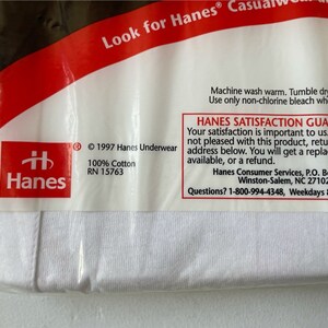 以下が含まれることがあります： 白いHanesの下着のパッケージ。パッケージには、赤いHanesのロゴ、「100％コットン」の文字、「Hanes Satisfaction Guarantee」の文字が含まれています。 パッケージは透明なプラスチックで密封されています。