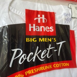 以下が含まれることがあります： 白いHanes Pocket-Tシャツがビニール袋に入っています。パッケージは赤、黒、白で、Hanesのロゴと「BIG MEN'S Pocket-T」の文字が印刷されています。シャツのサイズは2X、50-52です。