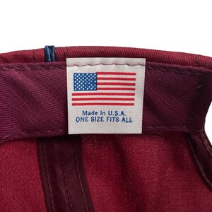 May include: A burgundy baseball cap with a white label that reads "Made in U.S.A. ONE SIZE FITS ALL" and features a small American flag.