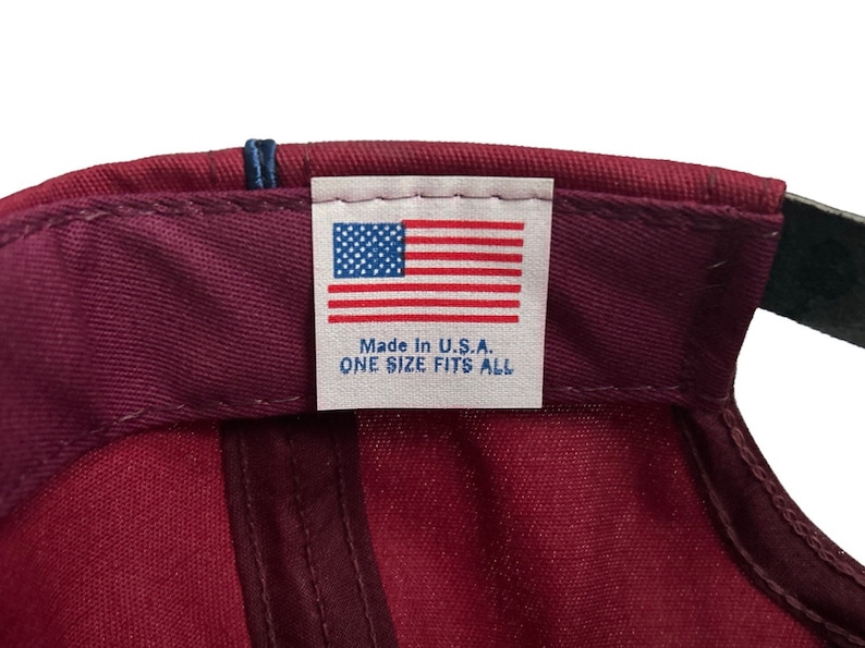 May include: A burgundy baseball cap with a white label that reads "Made in U.S.A. ONE SIZE FITS ALL" and features a small American flag.