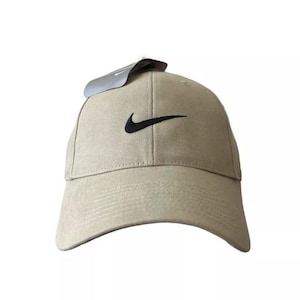 Può includere: Un cappello da baseball beige con un logo Nike swoosh nero ricamato sul davanti.