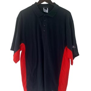 K&ouml;nnte beinhalten: Ein kurz&auml;rmeliges Poloshirt in Schwarz und Rot mit dem Schriftzug "Nike Golf" am Kragen.