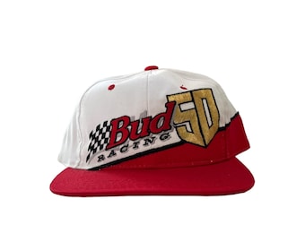 May include: White and red baseball cap with a Bud 50 Racing logo embroidered on the front. The logo is in red, black, and gold.