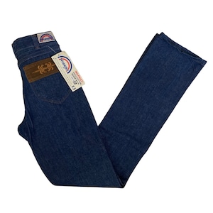 May include: A pair of blue denim jeans with a brown leather patch on the back pocket. The jeans have a rainbow-colored Wrangler label attached to the back pocket.