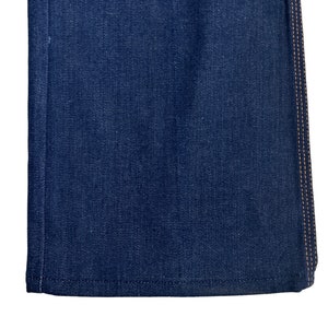 May include: Close-up of the bottom edge of a pair of dark blue denim jeans with a contrasting orange stitch detail.
