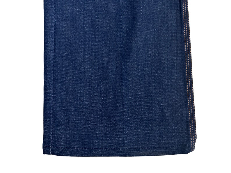 May include: Close-up of the bottom edge of a pair of dark blue denim jeans with a contrasting orange stitch detail.