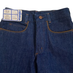 May include: A pair of dark blue denim jeans with a brown leather label that reads "Wrangler" and "27 x 36" and "Lancer Straight Leg Prewashed".