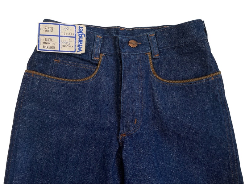May include: A pair of dark blue denim jeans with a brown leather label that reads "Wrangler" and "27 x 36" and "Lancer Straight Leg Prewashed".