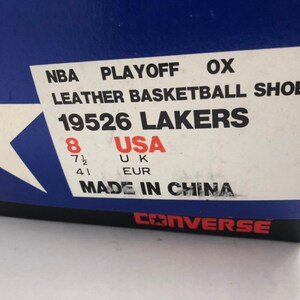 Puede incluir: Una caja blanca con ribete azul y una etiqueta blanca. La etiqueta dice "NBA PLAYOFF OX LEATHER BASKETBALL SHOES 19526 LAKERS" y enumera el tama&ntilde;o del zapato como "8 USA 7 1/2 UK 41 EUR". La etiqueta tambi&eacute;n dice "MADE IN CHINA". La parte inferior de la caja dice "CONVERSE" en letras negras.