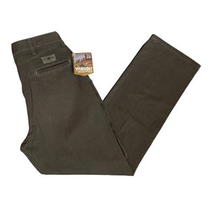 May include: A pair of dark green Wrangler Rugged Wear trousers with a tag attached. The tag is white with brown text and a picture of a man wearing the trousers.