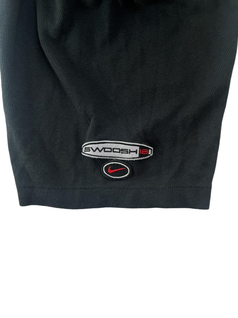 K&ouml;nnte beinhalten: Schwarzes Sport-Shirt mit einem wei&szlig;en und roten "SWOOSH18"-Logo unten rechts.